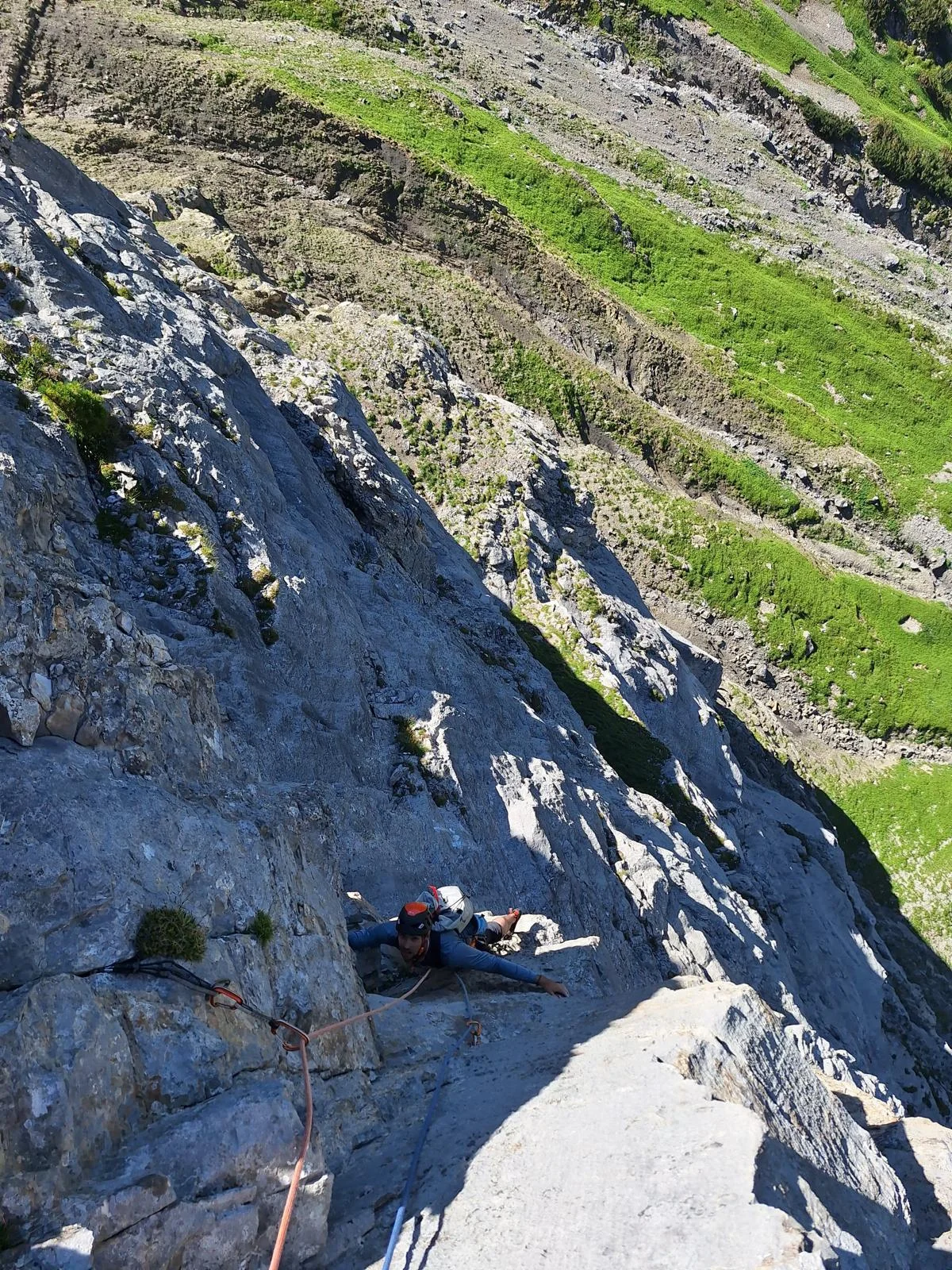 Tiefblick auf einen Kletterer im Kalkfels über den grünen Hängen an der Rot Spitz.