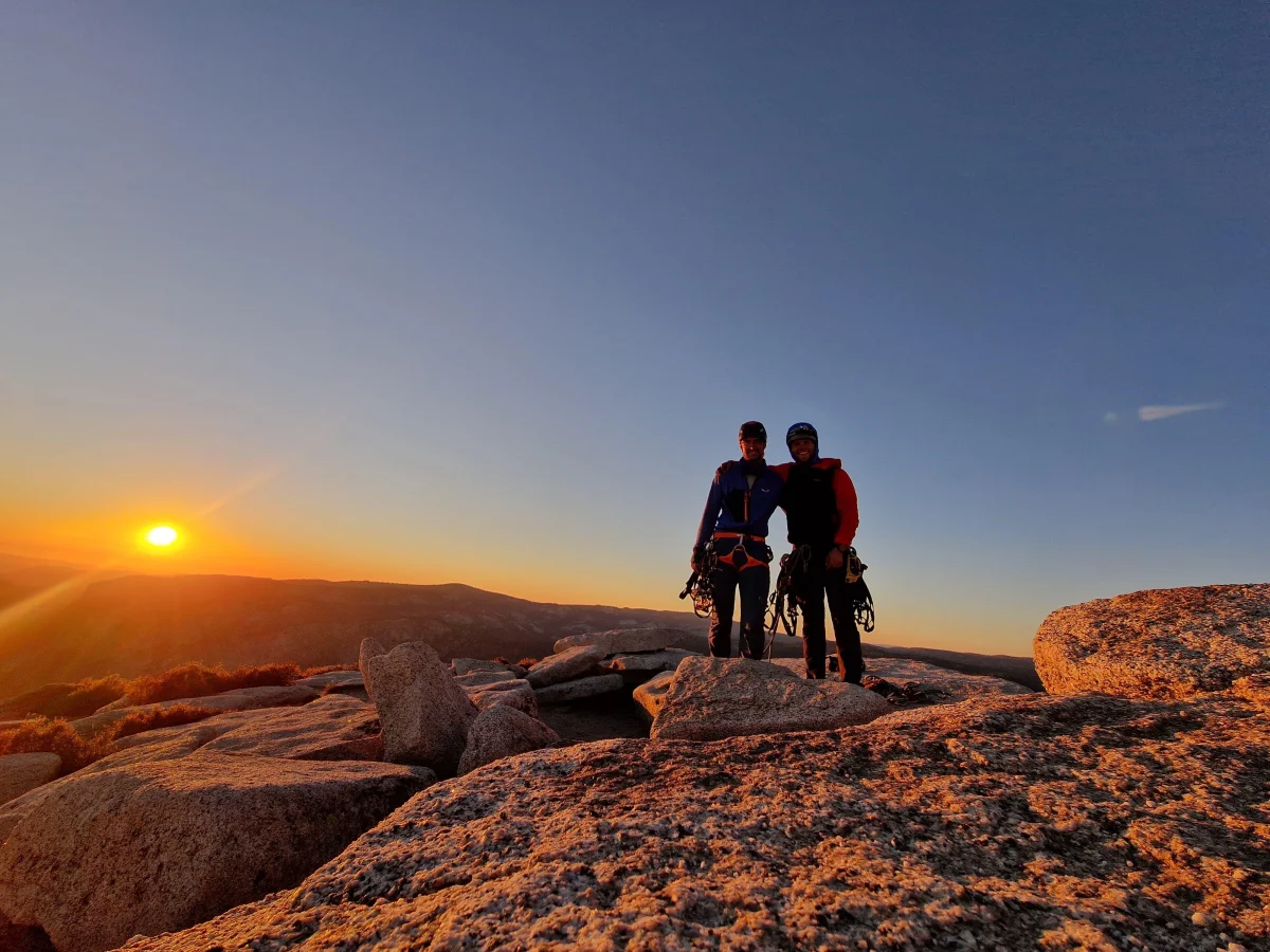 Zwei Bergsteiger auf dem Gipfelplateau des Half Dome bei Sonnenuntergang.