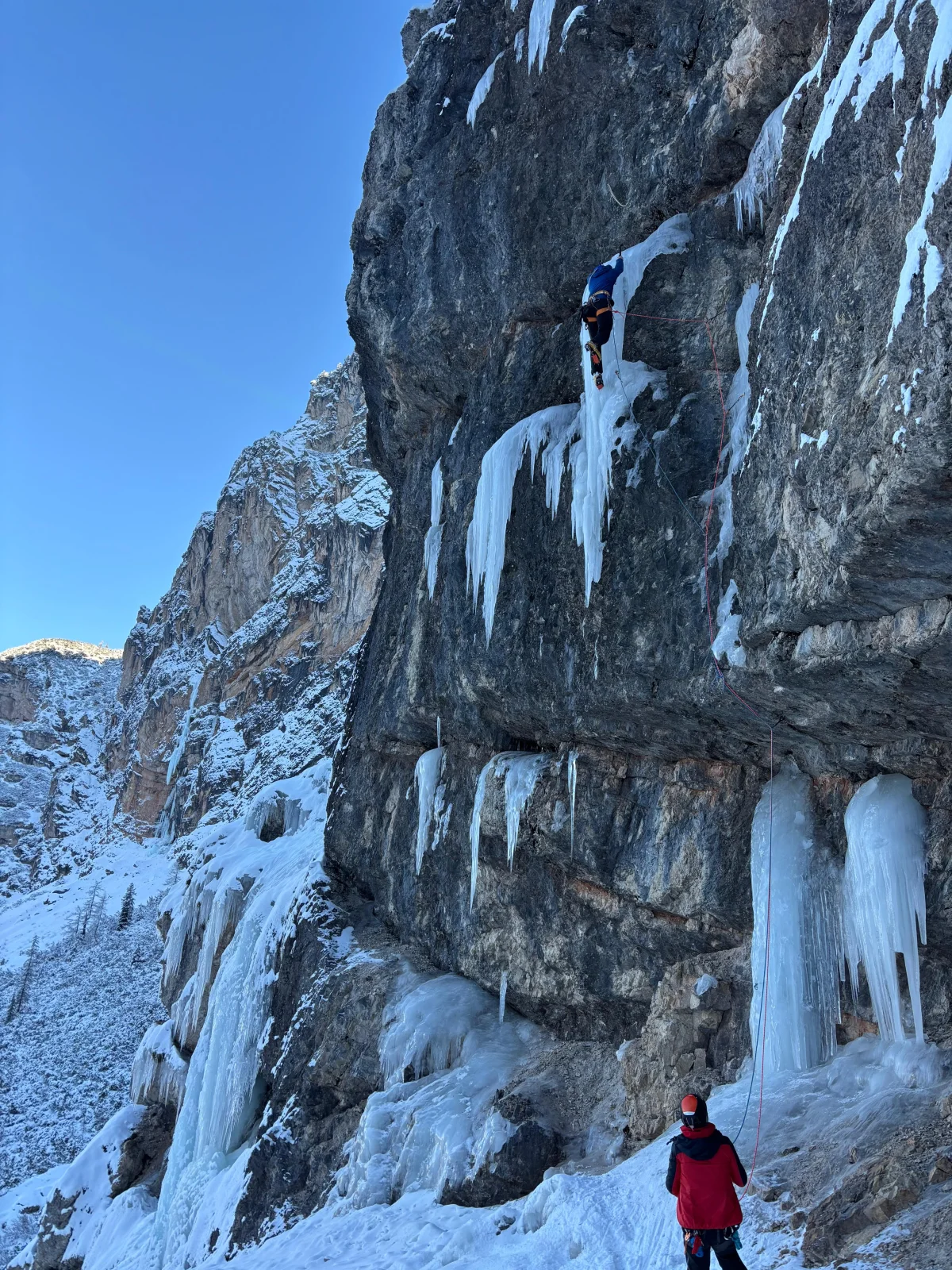 Eiskletterer unter einem gefrorenen Wasserfall an einer steilen Felswand.