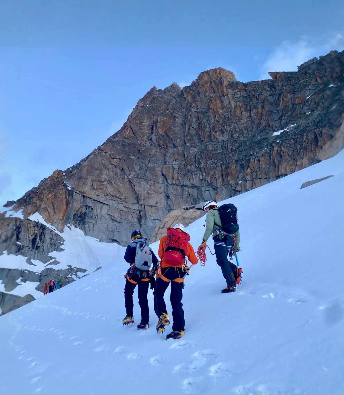 Seilschaft mit Rucksäcken beim Aufstieg über einen Schneehang.