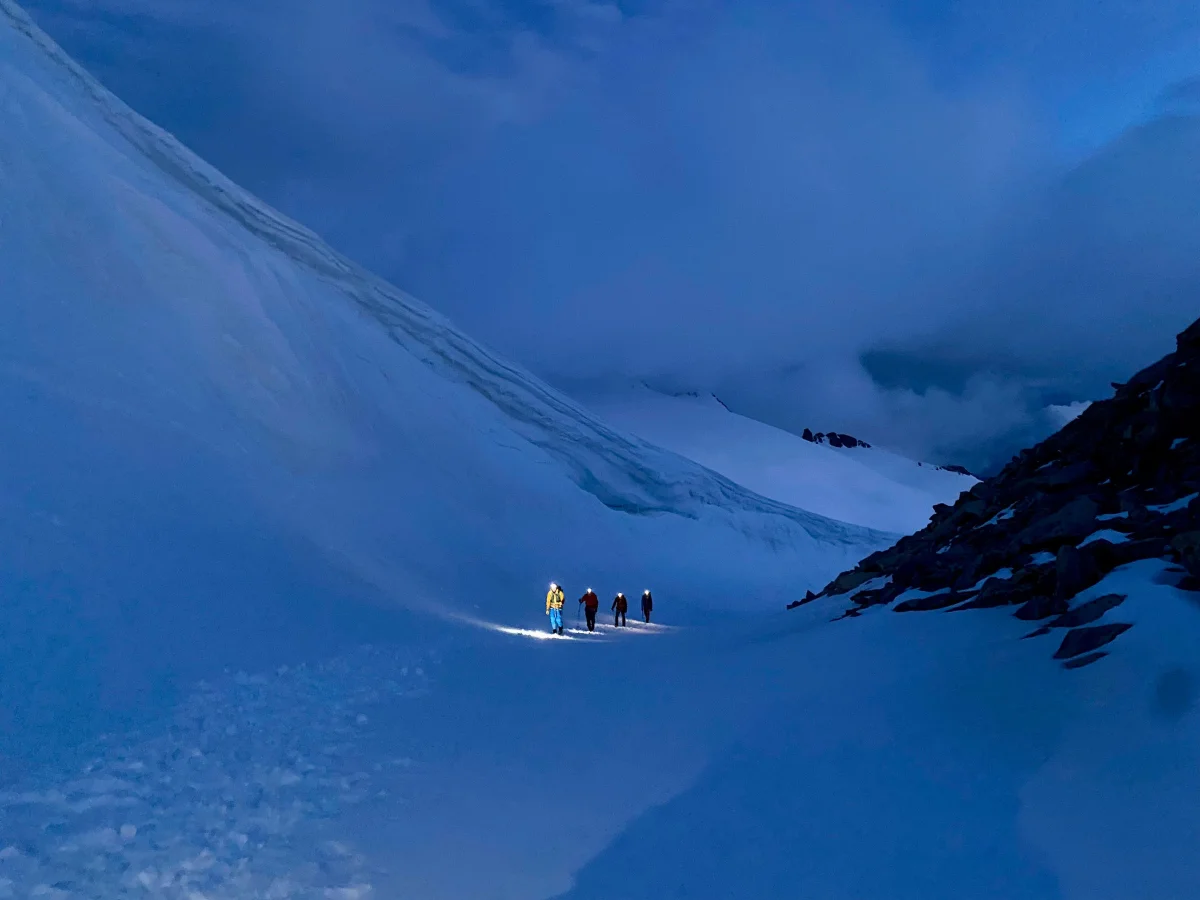 Mountaineers with headlamps ascending through a snowy mountain landscape.