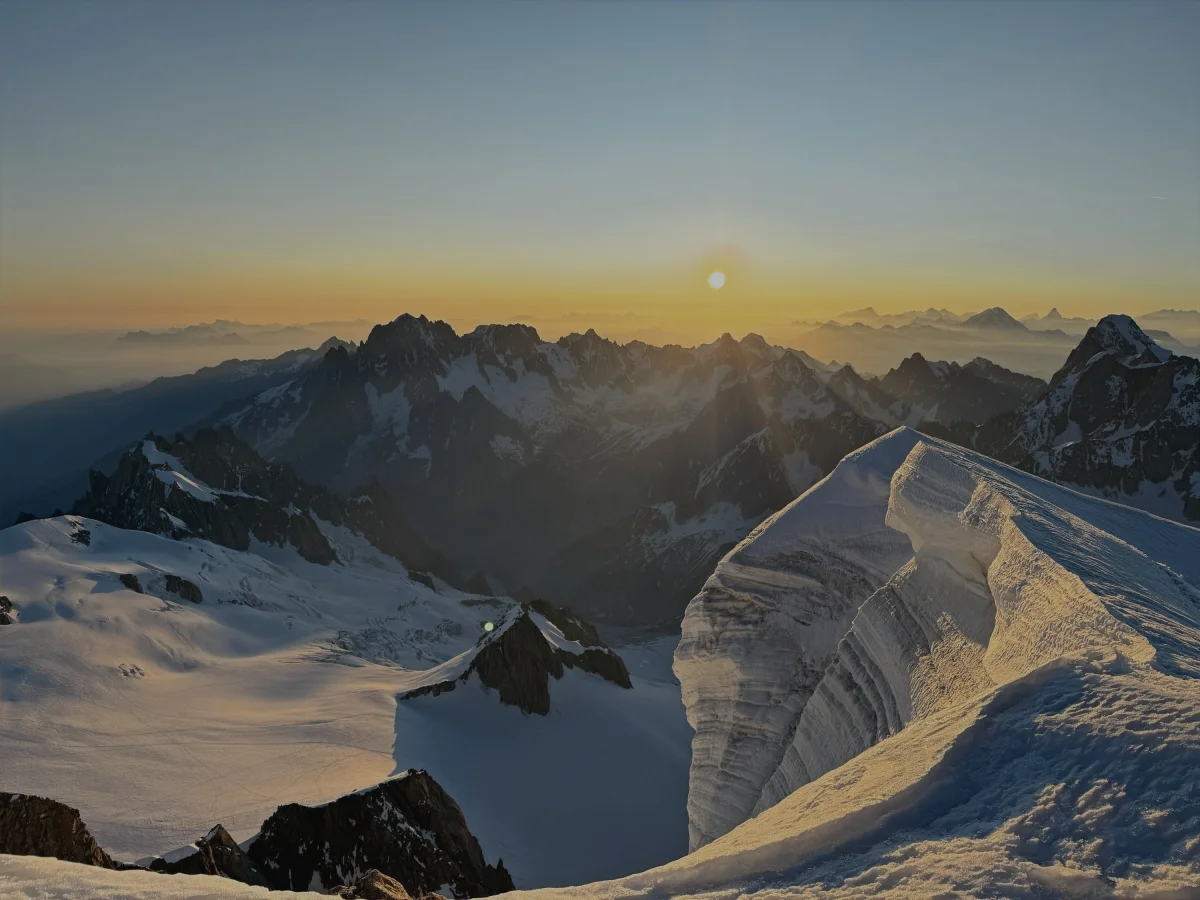 Sunrise over snowy peaks and a narrow snow ridge.