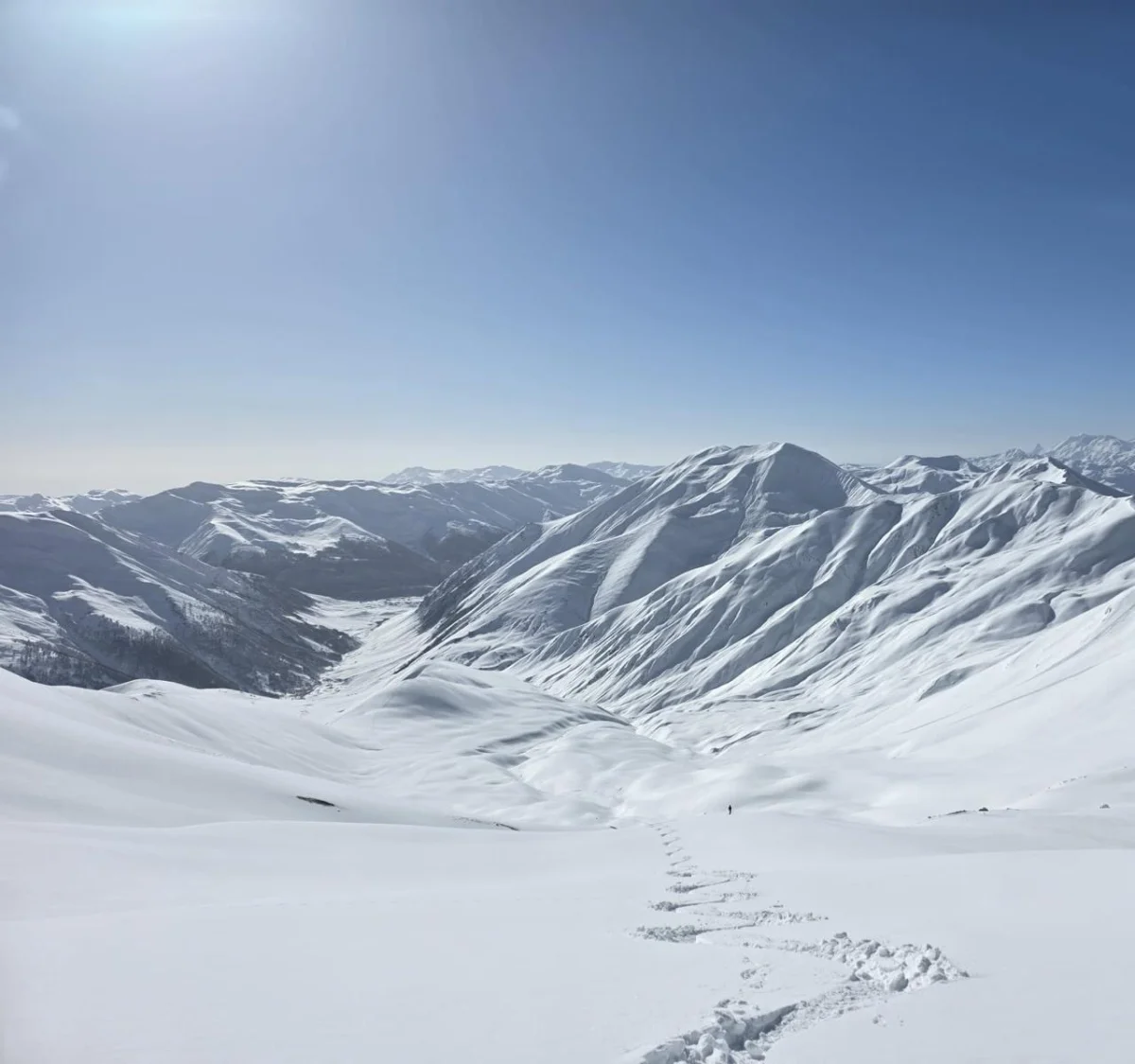 Verschneites Gebirgstal mit einer einzelnen Skispur unter blauem Himmel.