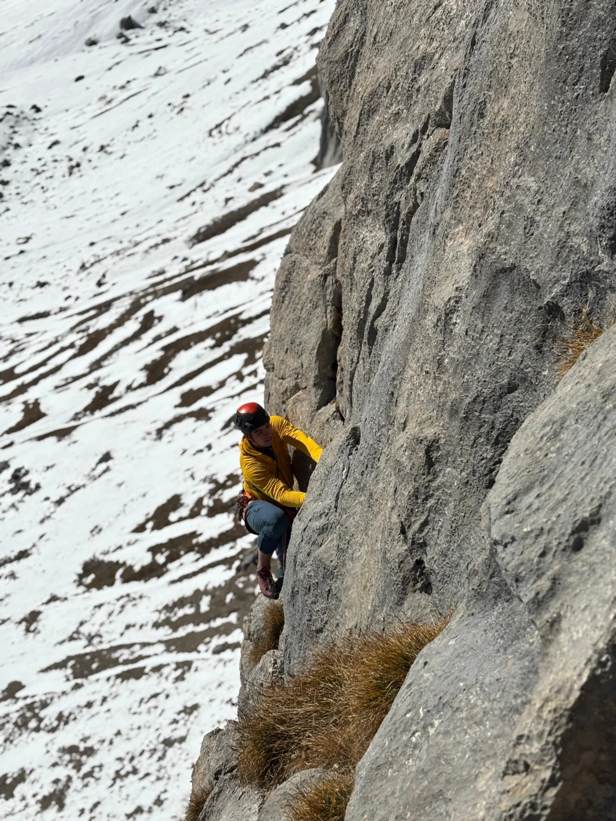Climber in a yellow jacket on a steep rock face during an alpine climb at Arlberg and in the Lechquellen Mountains.