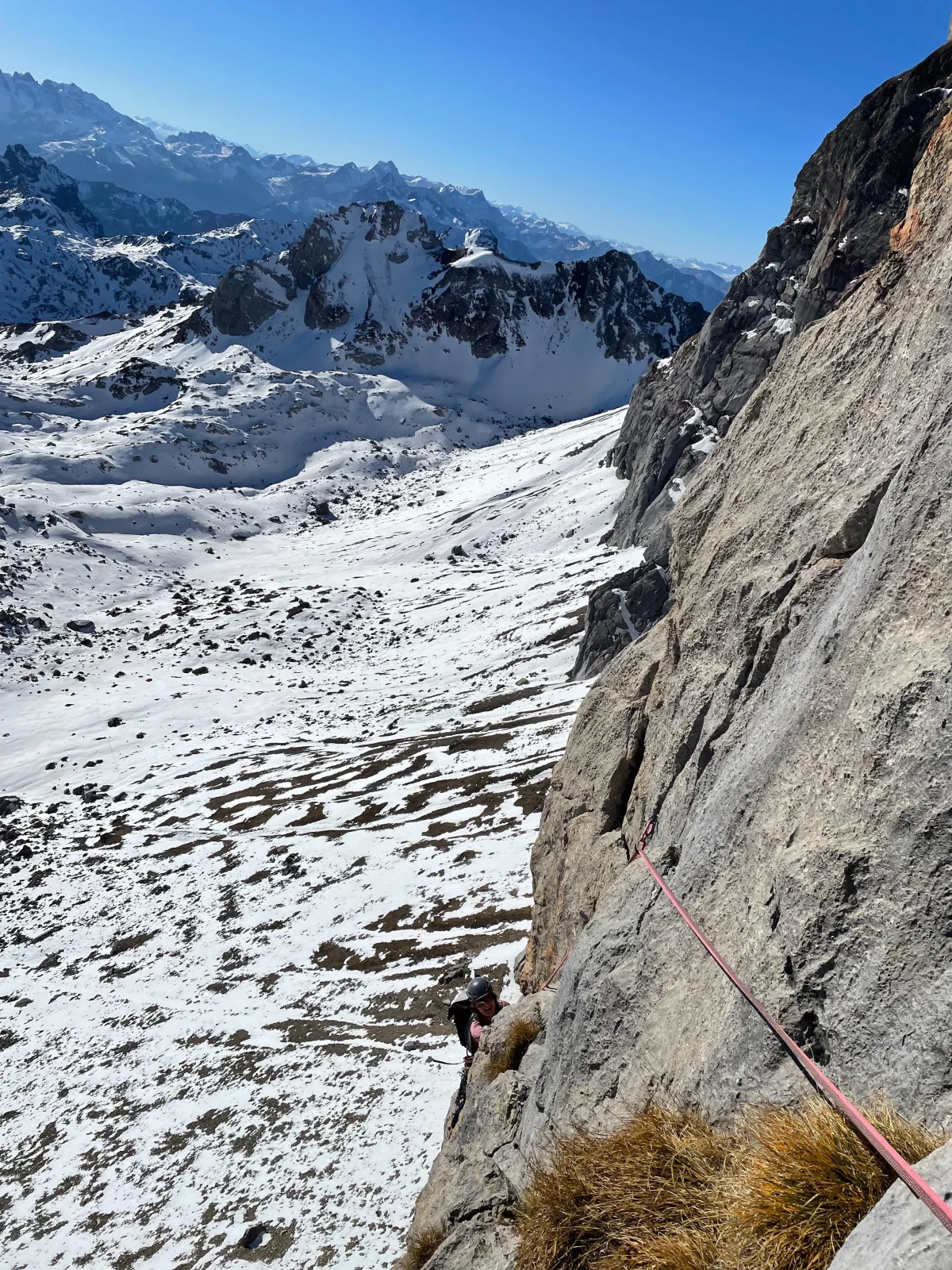 Kletterin am Seil in einer steilen Felswand mit Blick auf verschneite Berge.