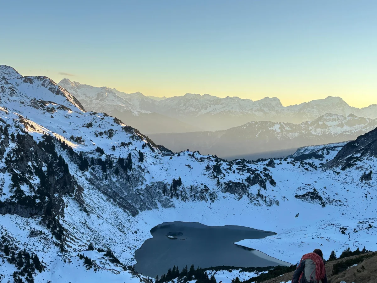 Abstieg mit Rucksack und Kletterseil oberhalb eines Bergsees in verschneiter Berglandschaft.