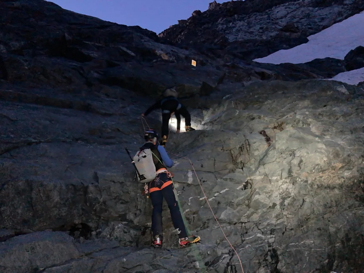 Biancograt on Piz Bernina: Mountaineers with headlamps on a rocky approach in darkness.