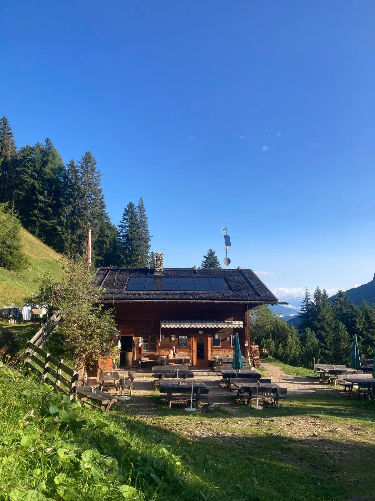 Burgstallkante – Dolomite Classic with Mountain Guide: Mountain hut on a sunny meadow beside a forest.