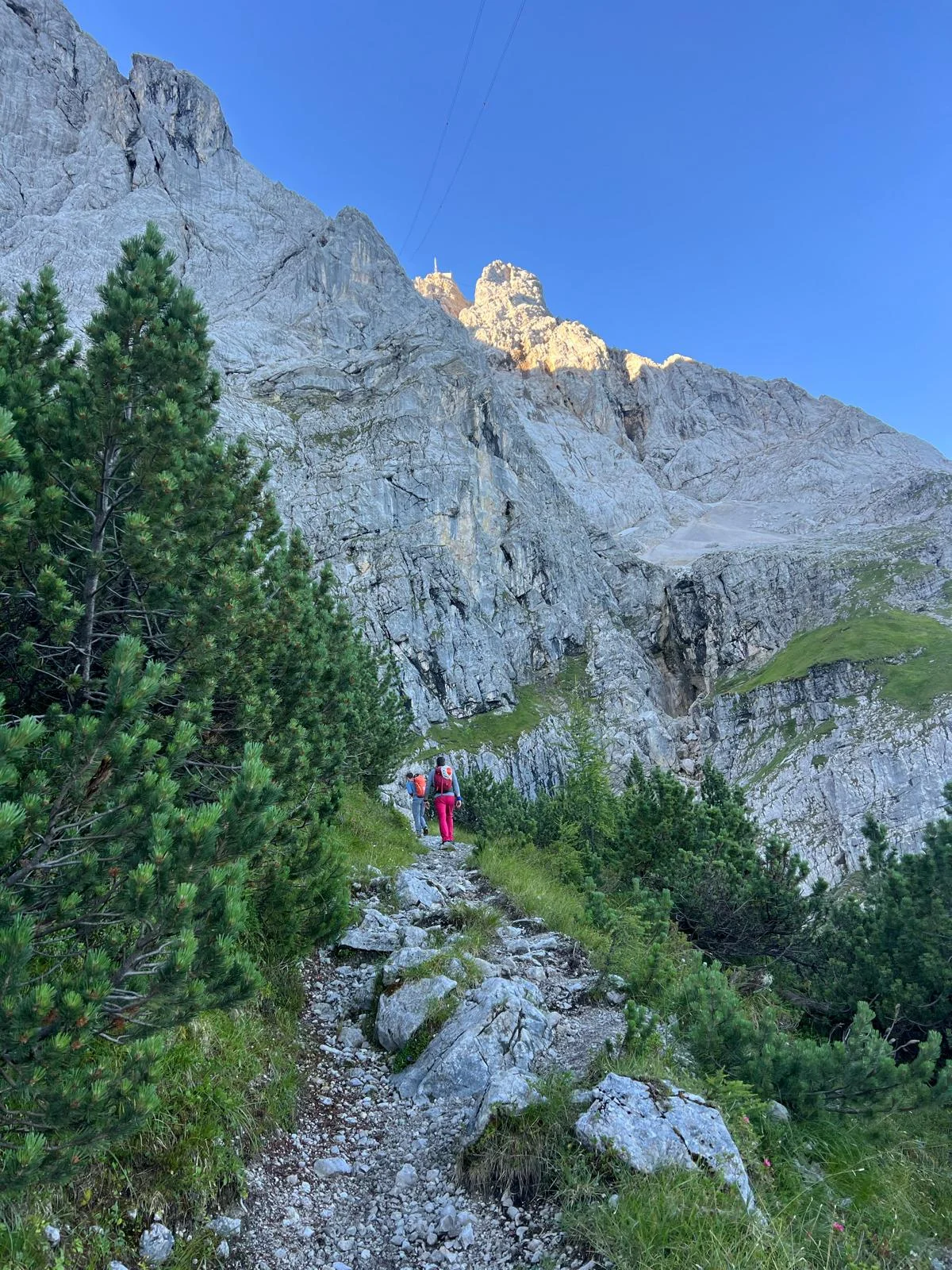 Eisenzeit – Zugspitze North Face: Mountaineers on an approach between forest and rock wall.