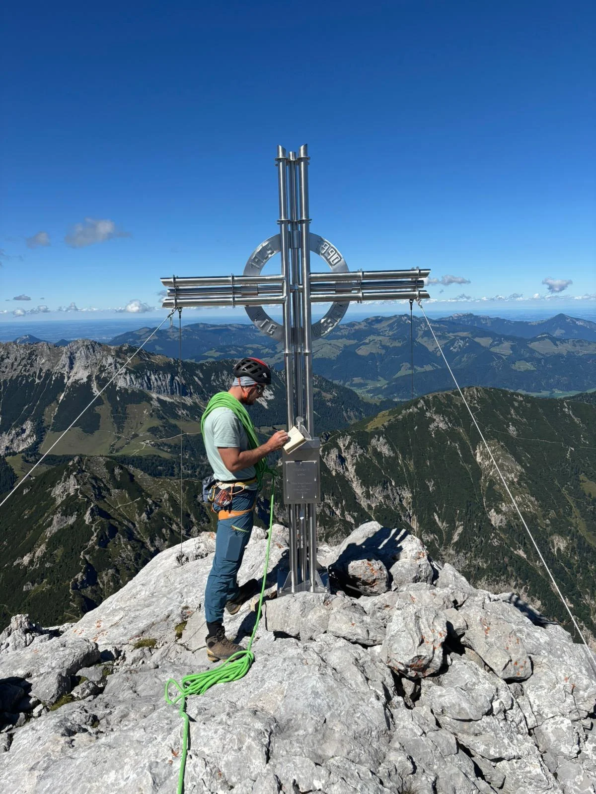 Fleischbank East Face – Dülfer Route: Mountaineer at a summit cross overlooking the surrounding mountains.