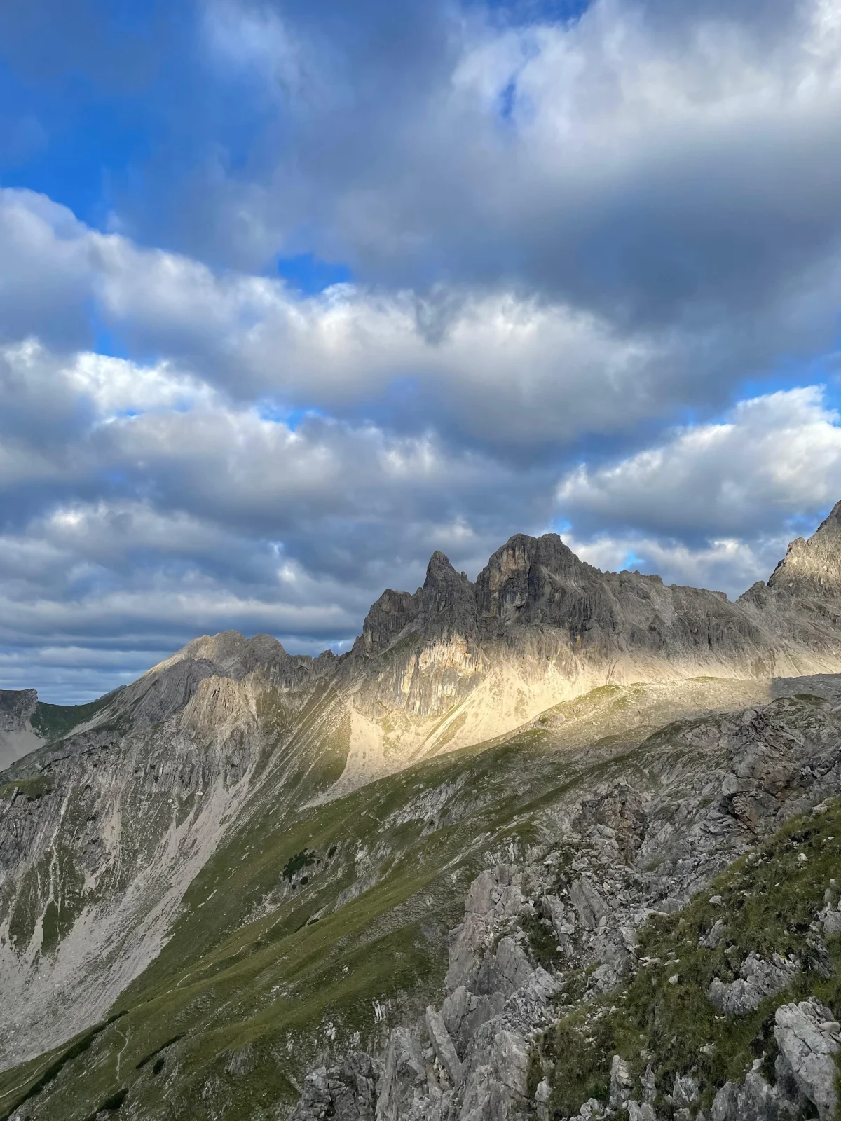 Sunlit rock towers above an alpine meadow beneath a cloudy sky.