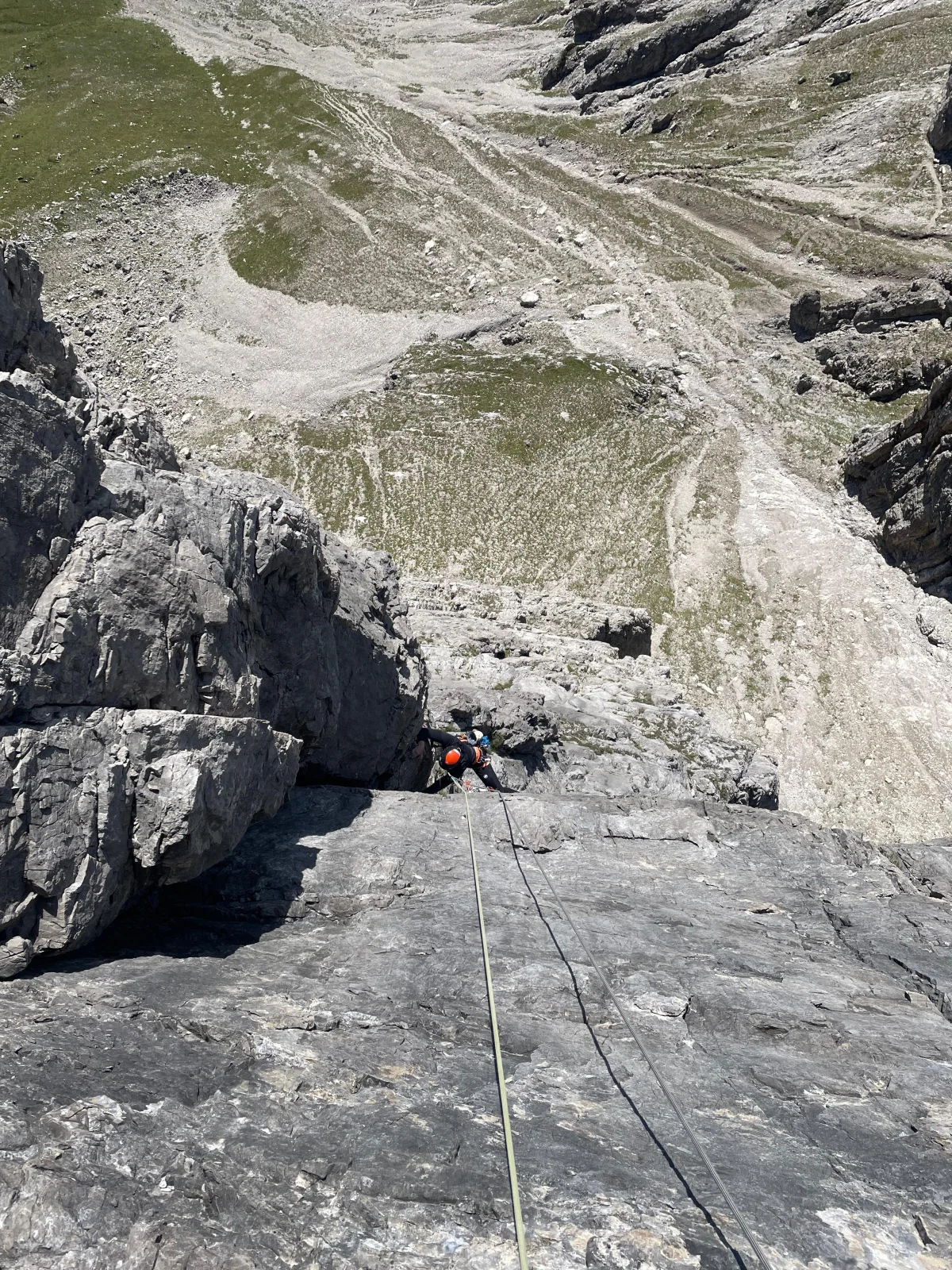 Roped climber on a rock slab above an alpine scree slope.