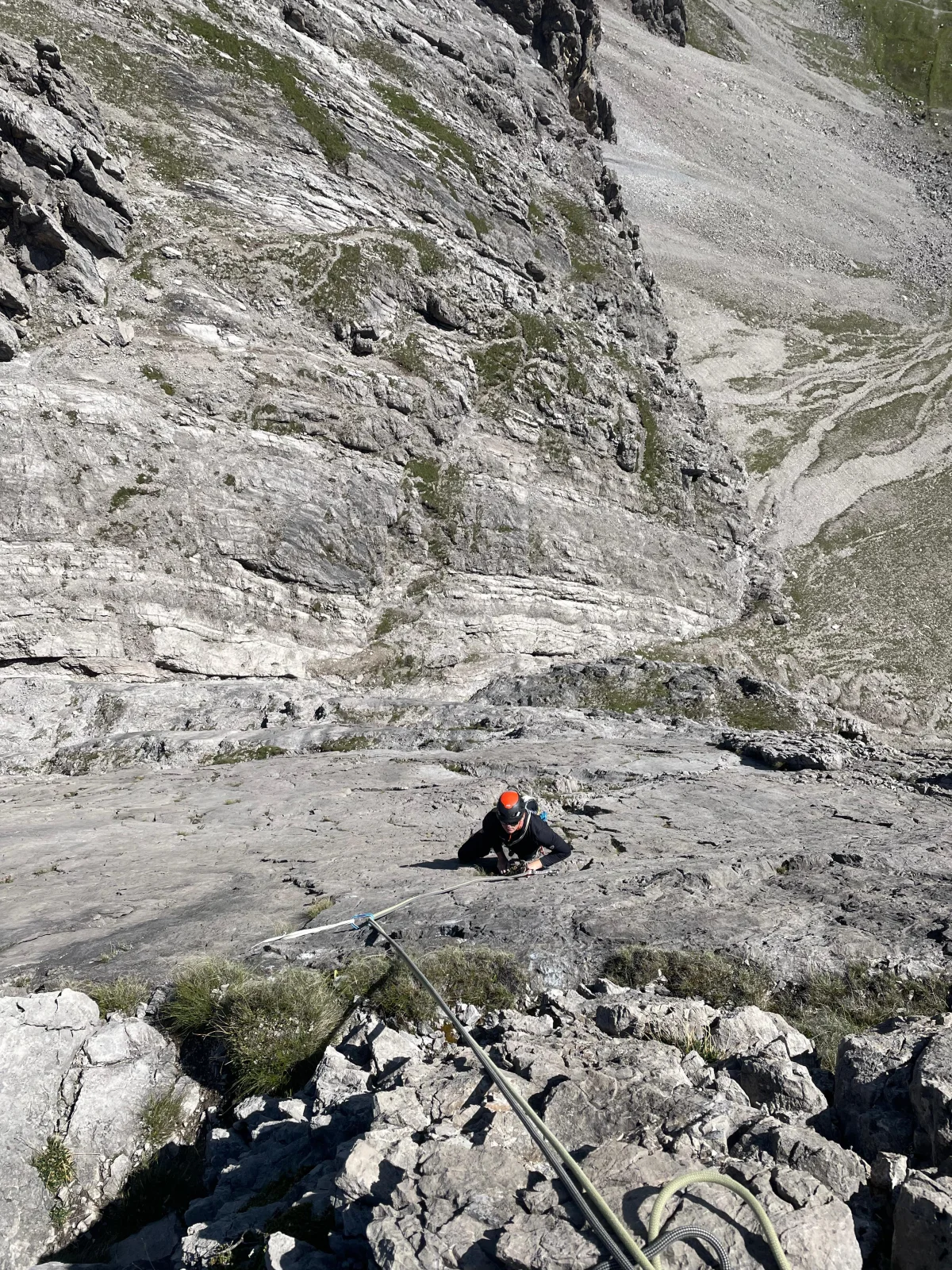 Climber wearing an orange helmet following a rope up a limestone wall.