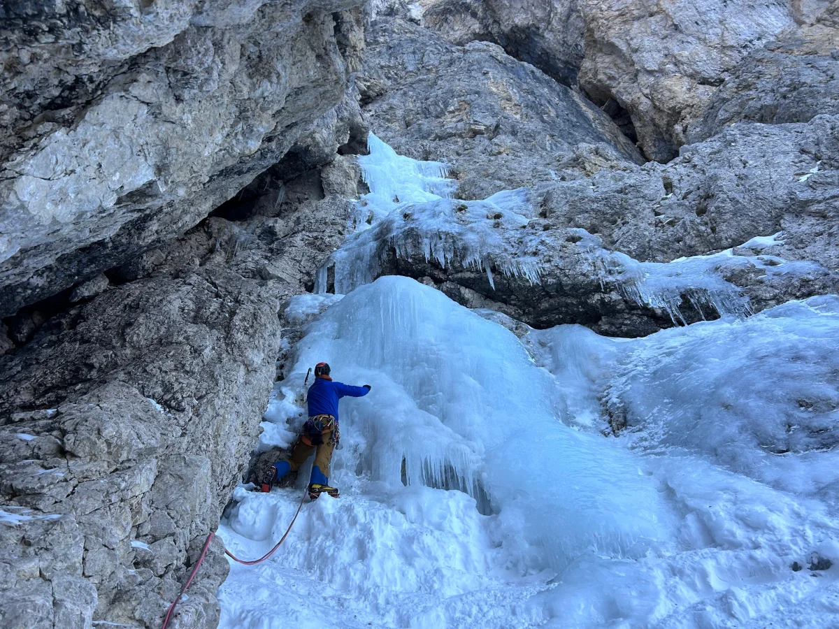 Hurschka – Val Mezdi – Guided Mixed Climbing Tour: Climber in a blue jacket on a stepped ice wall.