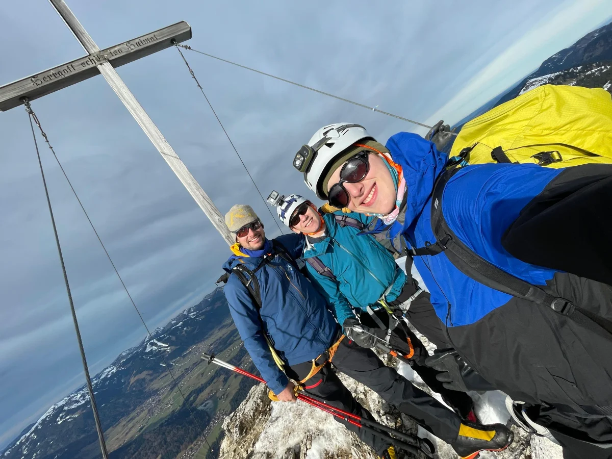Drei Bergsteiger mit Helm und Steigeisen am Gipfelkreuz des Rubihorns nach der Durchsteigung der Nordwand.