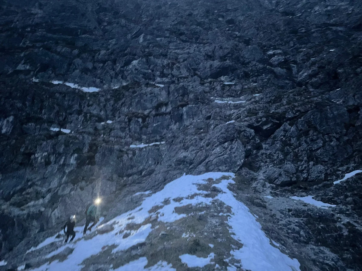 Bergsteiger mit Stirnlampen bei Dunkelheit im Zustieg über ein Schneefeld unter der Rubihorn-Nordwand.