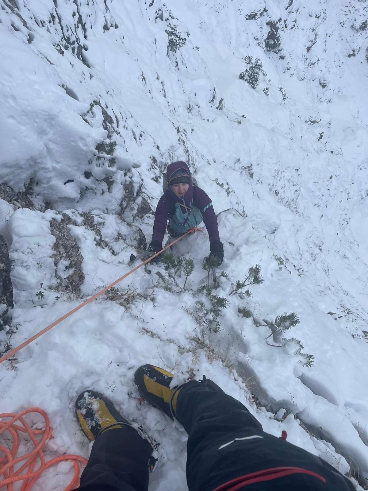 Blick vom Standplatz auf eine nachsteigende Bergsteigerin im verschneiten, steilen Gelände der Nordwand.