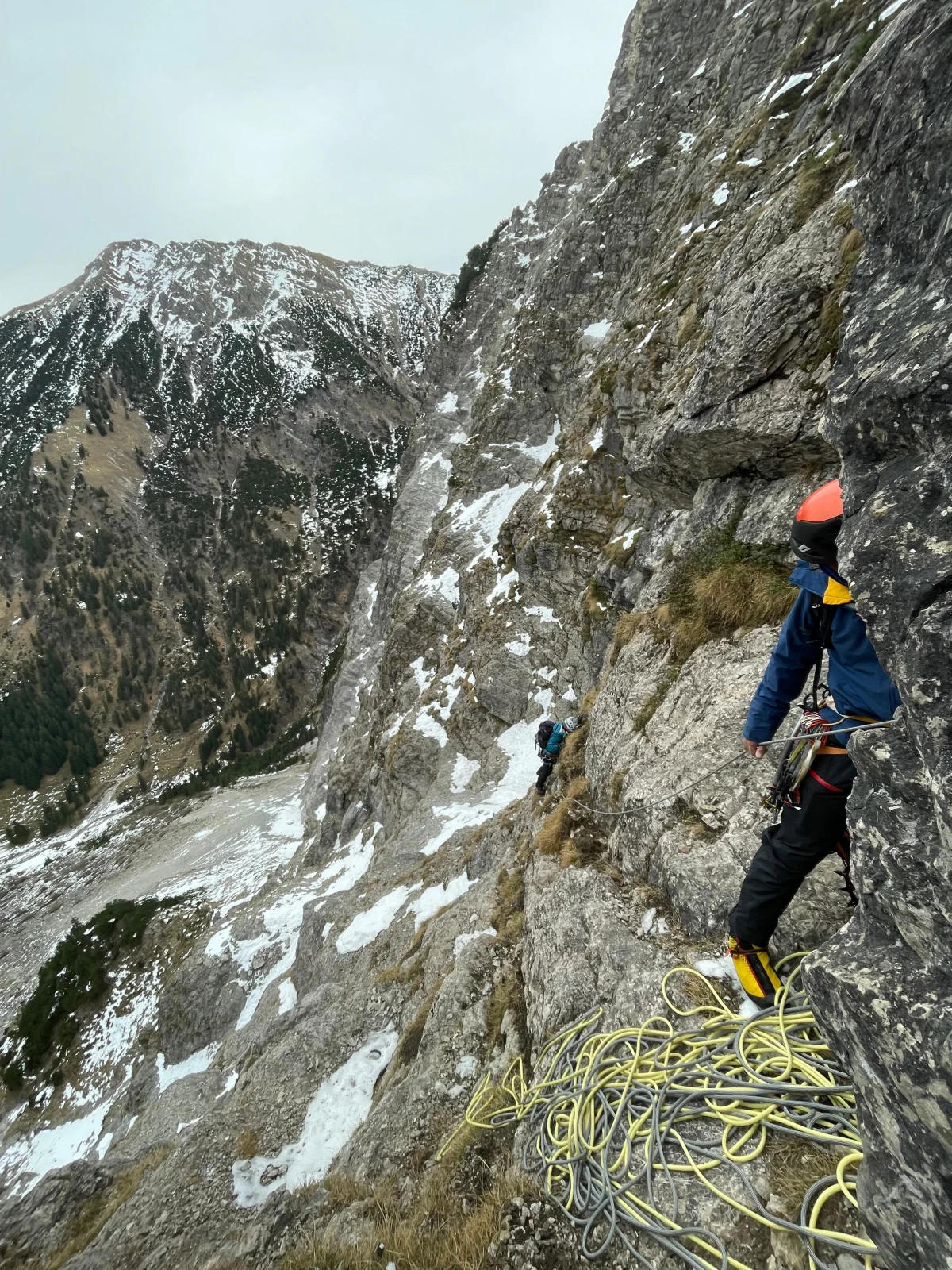Bergsteiger mit Helm und Seil auf einem Felsband in der Rubihorn-Nordwand, gegenüber verschneite Allgäuer Gipfel.