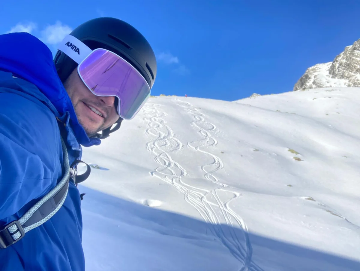 Ski Touring in Sellrain with a Mountain Guide: Smiling skier with purple goggles in front of ski tracks.