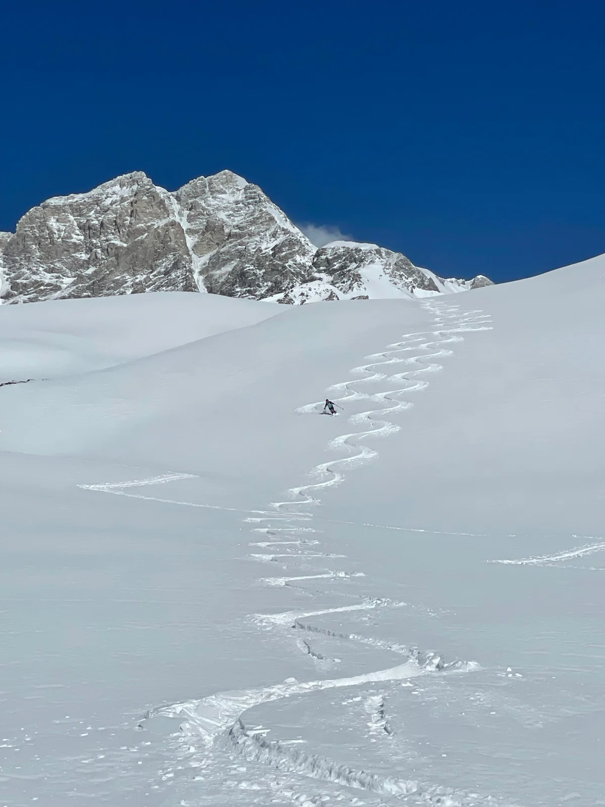 Skitouren in Georgien - Ushguli - Svanetien: Geschwungene Skispuren vor einem felsigen Berggipfel.