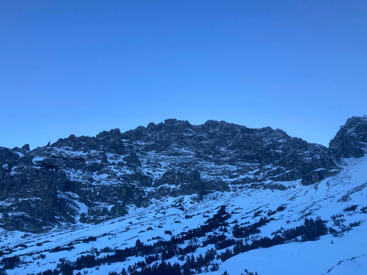 Winter Mountaineering on Thaneller: Snow-covered rocky mountainside beneath a blue sky.